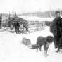 Photograph of Frank Higgins and a dog with a sled outside a lumber camp c.1900.