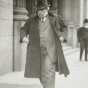 Black and white photograph of James J. Hill walking down street with overcoat flapping, c.1915.