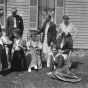 Black and white photograph of Sinclair Lewis and friends, ca. 1916. Lewis sits in the rocking chair at right; his wife, Grace Hegger Lewis, wears a maid’s uniform and stands at left.