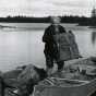 Black and white photograph of Dorothy Molter lifting a pack out of a canoe, Isle of Pines, Knife Lake, Boundary Waters Canoe Area, ca. 1960s.