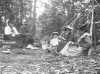 Black and white photograph of Frances Densmore seated on ground with others at Pigeon River, c. 1905.