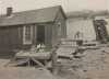 Black and white photograph of a shack and outhouse, river’s edge, 1917