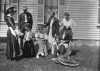 Black and white photograph of Sinclair Lewis and friends, ca. 1916. Lewis sits in the rocking chair at right; his wife, Grace Hegger Lewis, wears a maid’s uniform and stands at left.