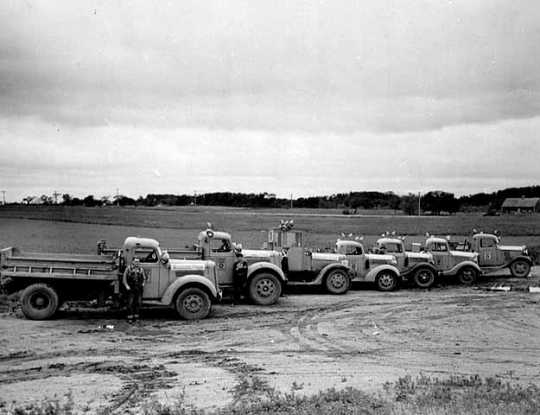 Black and white photograph of highway trucks delivering grasshopper poison to farmers, 1938. 